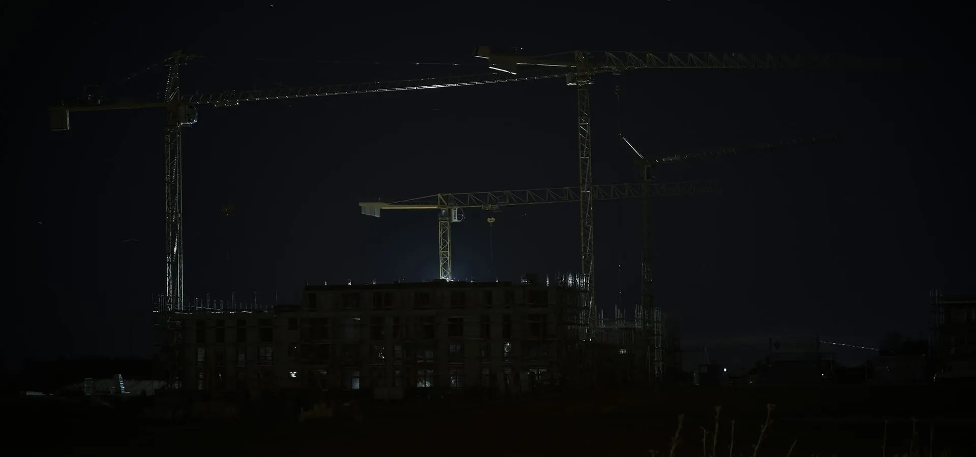 Tower cranes over a construction site lit against a dark night sky.